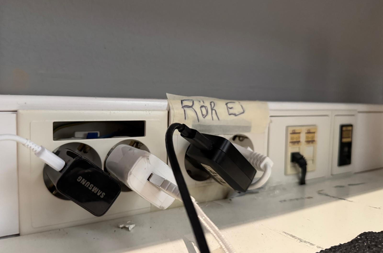 Handskriven lapp med texten RÖR EJ tejpad ovanför ett vägguttag
